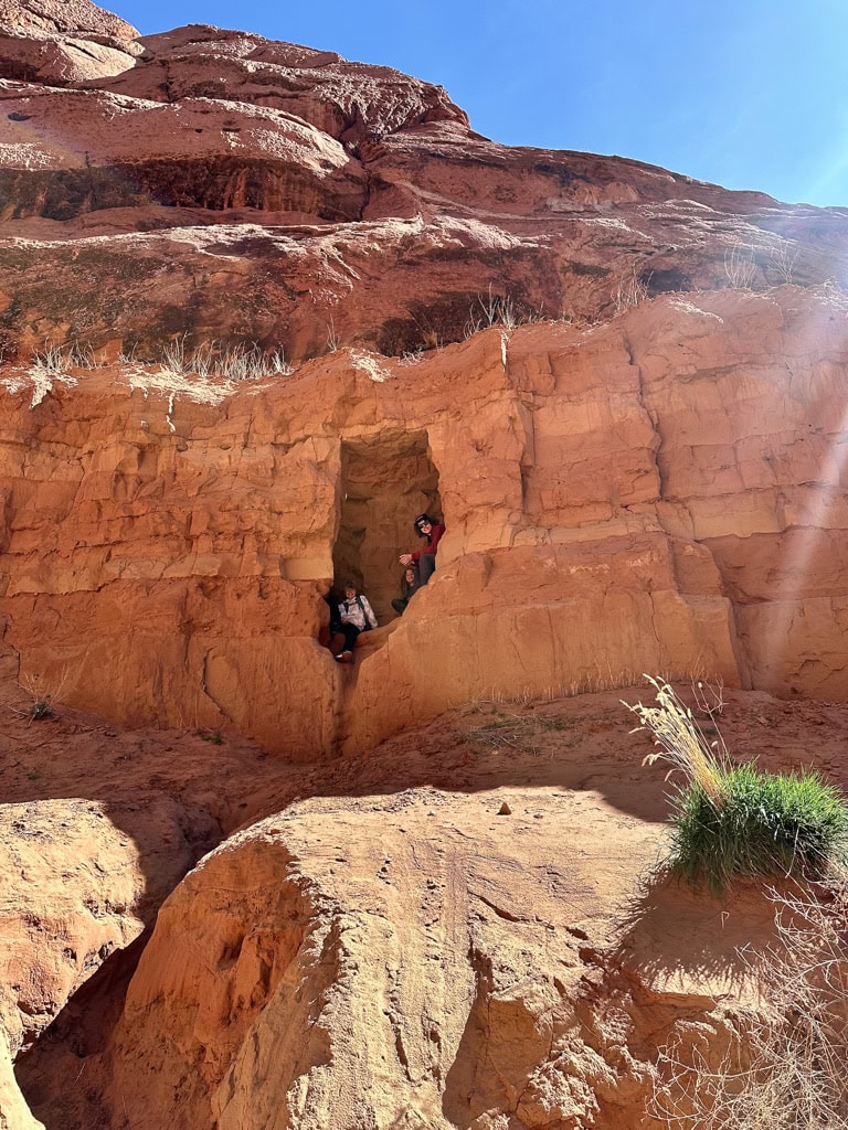 Two male cousins sitting in a red rock alcove during a slot canyon hike in Utah.